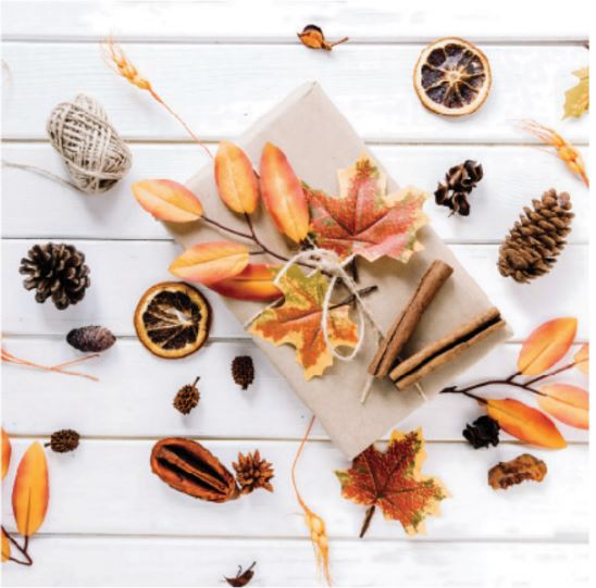 Autumn-themed arrangement with leaves, oranges, cinnamon sticks, and pine cones on a white wooden surface.